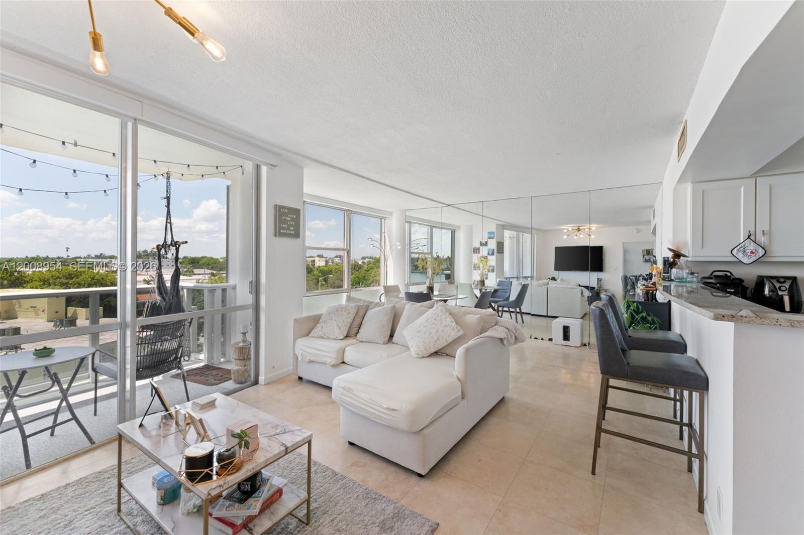 A bright living room features a white sectional sofa, mirrored walls, and a balcony with seating — 900 Bay Dr # 421, Miami Beach FL 33141, MIAMI BEACH, FL