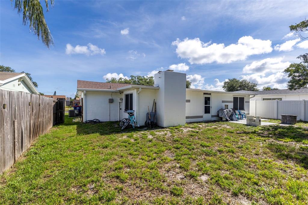 The backyard of a white house features a chimney, a bicycle, and a wooden fence — 3334 COLDWELL DRIVE, HOLIDAY, FL