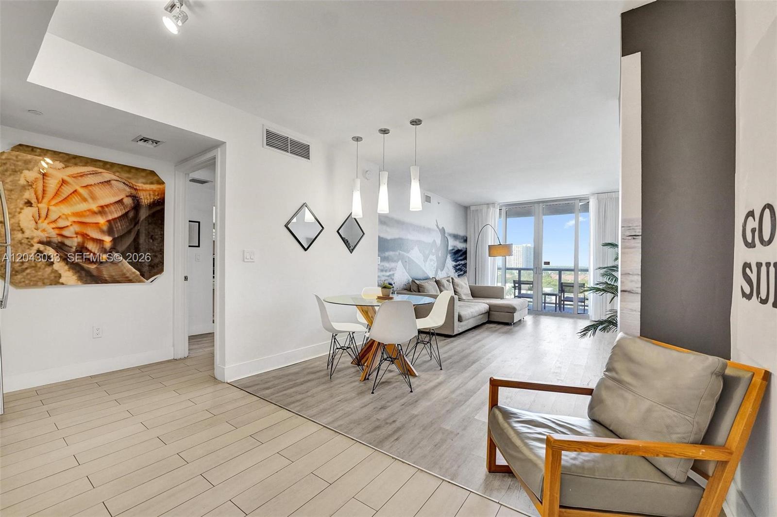 An open-concept living and dining area features light wood flooring, modern furniture, and balcony access — 2602 E Hallandale Beach Blvd # R906, Hallandale Beach FL 33009, HALLANDALE BEACH, FL