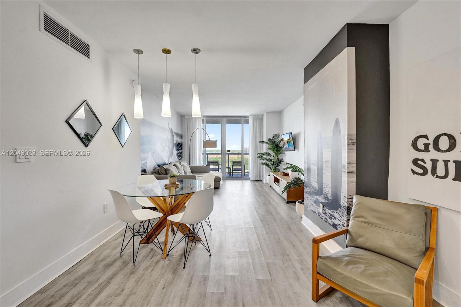 A modern living and dining area features light wood floors, glass furniture, and balcony access — 2602 E Hallandale Beach Blvd # R906, Hallandale Beach FL 33009, HALLANDALE BEACH, FL