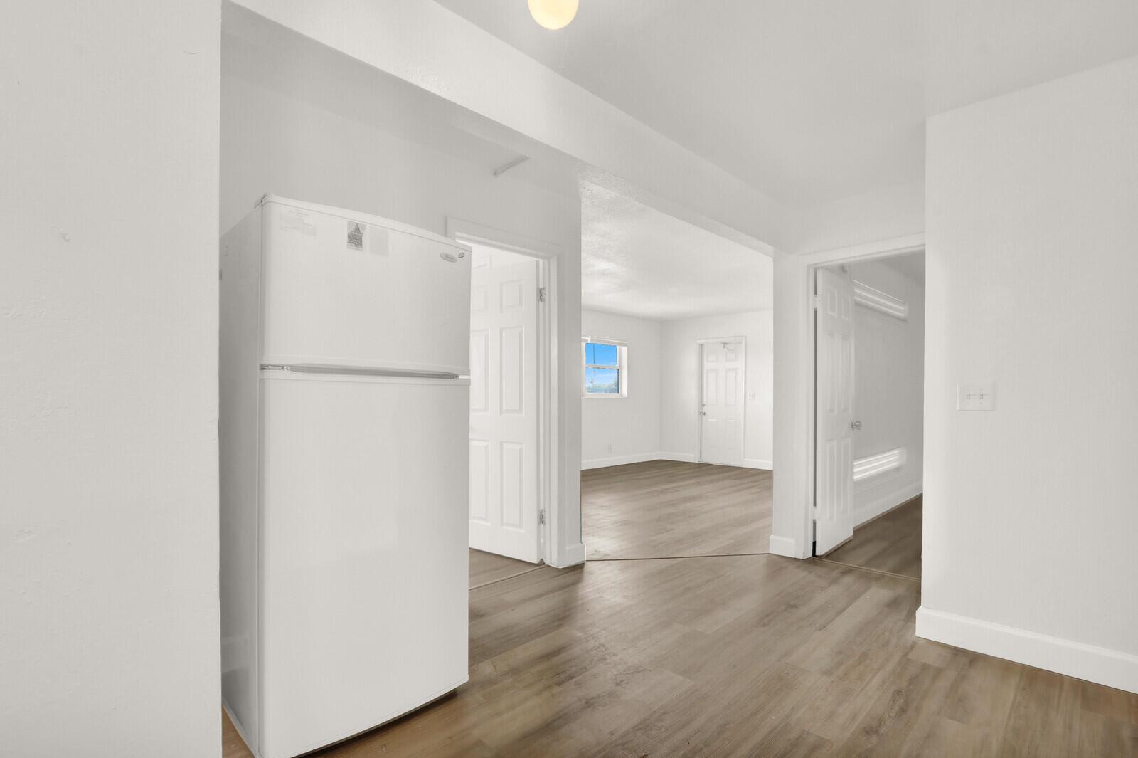 A white refrigerator stands in a room with light wood-look flooring and open doorways — 2701 Avenue E, Riviera Beach FL 33404, RIVIERA BEACH, FL