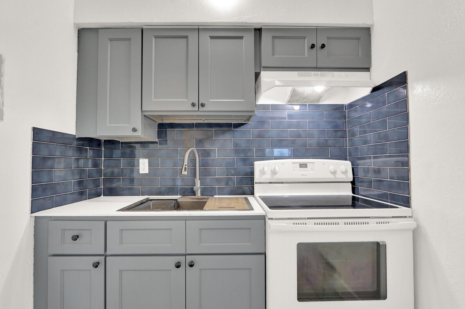 A kitchen features gray cabinets, a white stove, and a blue subway tile backsplash — 2701 Avenue E, Riviera Beach FL 33404, RIVIERA BEACH, FL