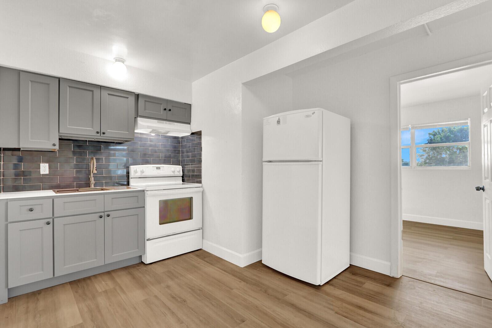 A kitchen features gray cabinets, a white stove, a white refrigerator, and dark subway tiles — 2701 Avenue E, Riviera Beach FL 33404, RIVIERA BEACH, FL