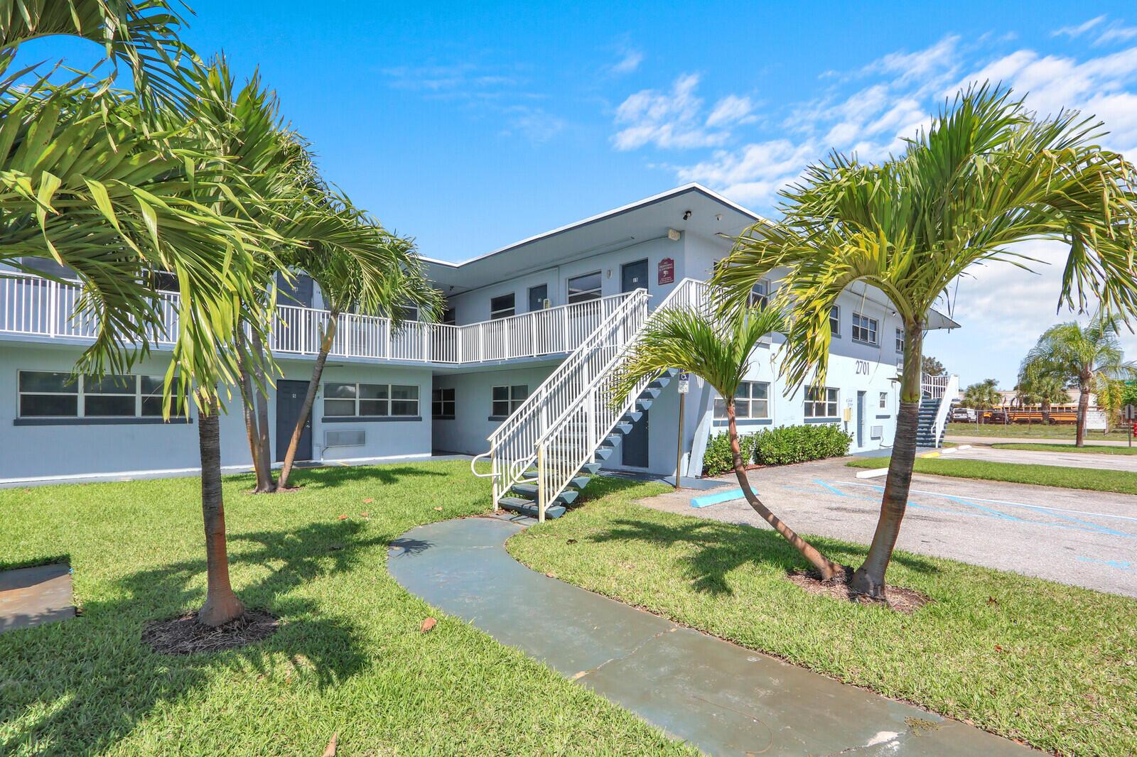 An exterior view of a two-story apartment building with palm trees and a staircase — 2701 Avenue E, Riviera Beach FL 33404, RIVIERA BEACH, FL