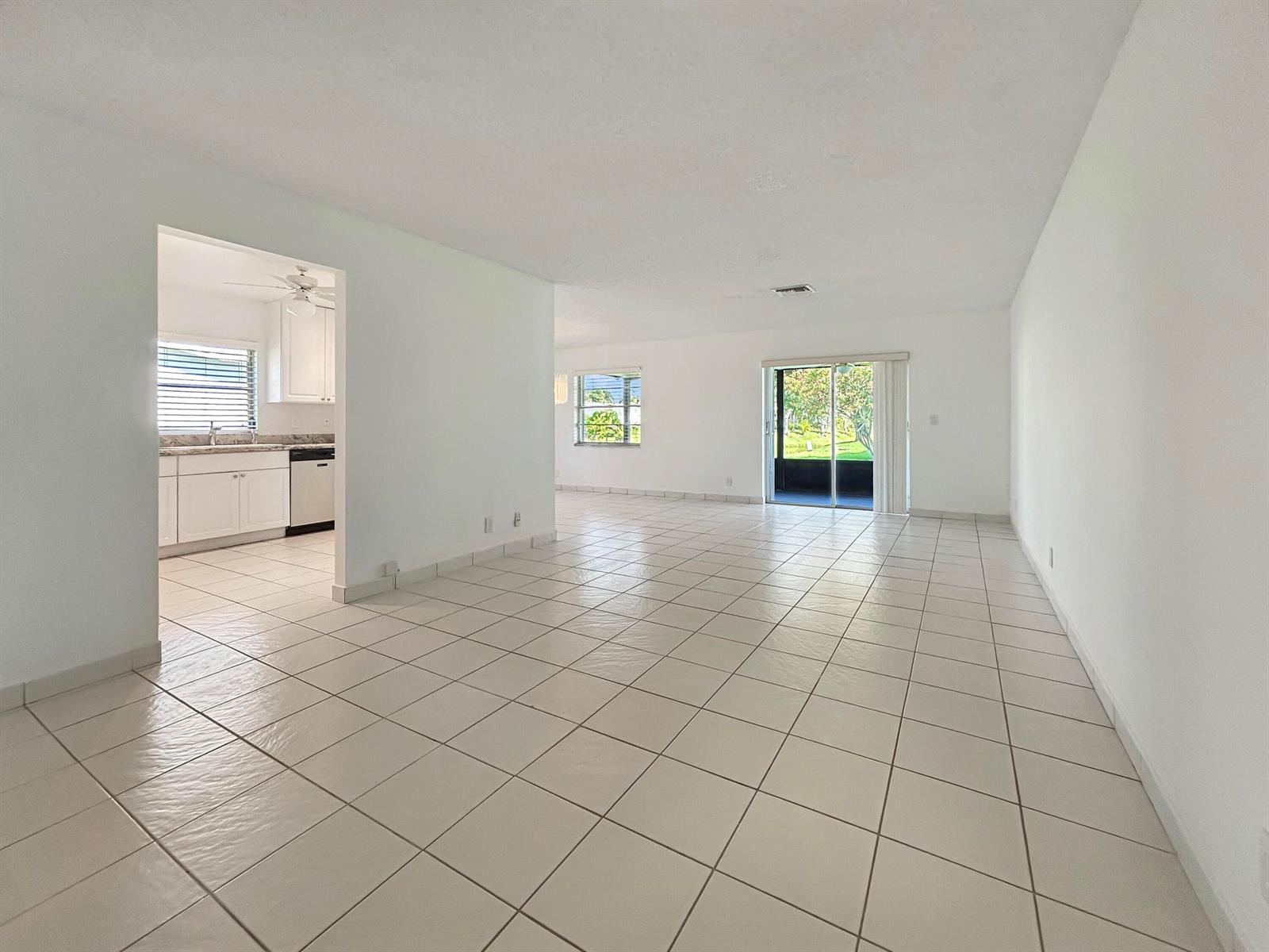 An open-concept living area with white tile floors, white walls, and an adjacent kitchen — 6091 Dusenburg Road, Delray Beach FL 33484, DELRAY BEACH, FL