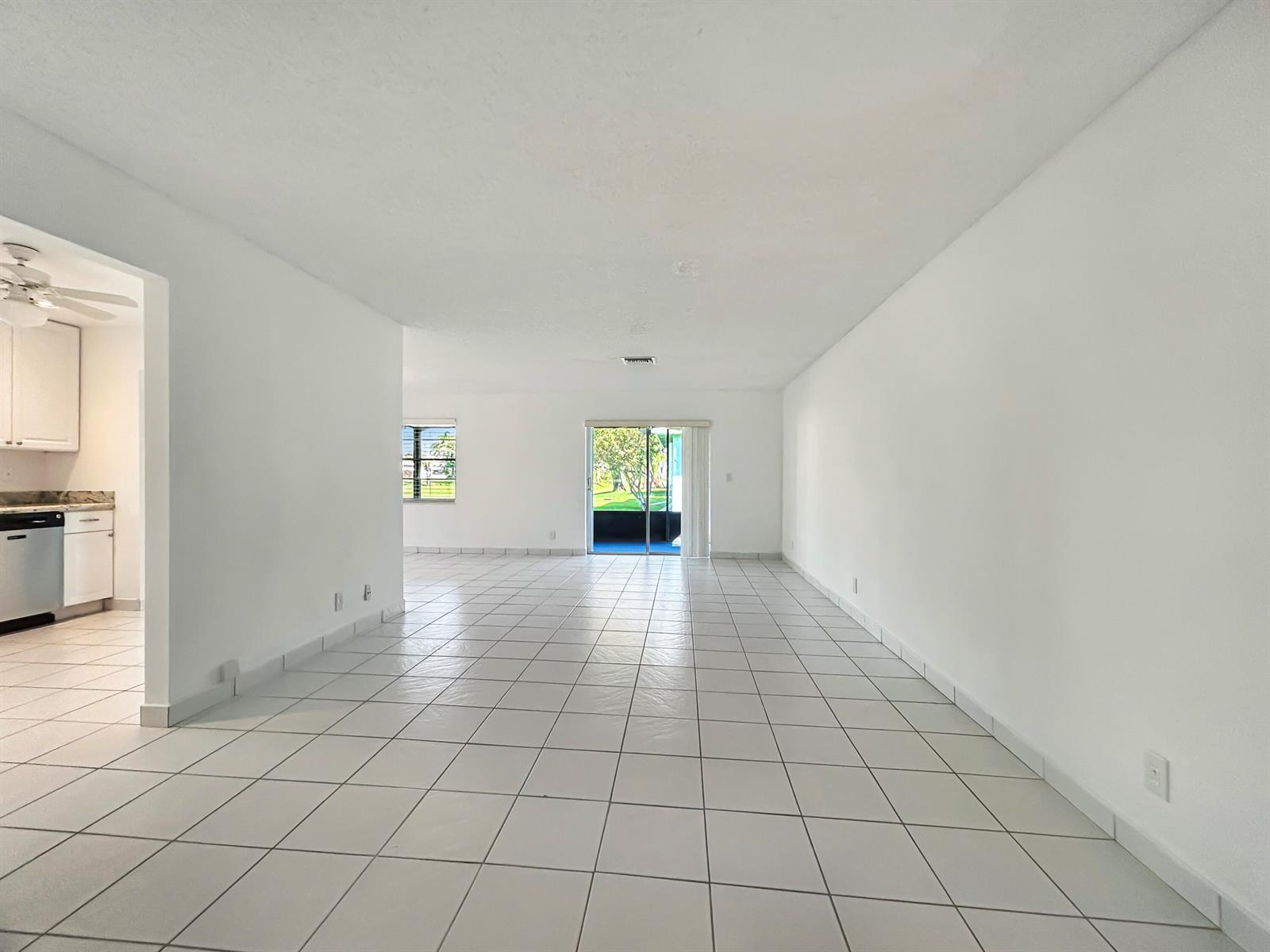 An empty living area with white walls, white tile flooring, and a sliding glass door — 6091 Dusenburg Road, Delray Beach FL 33484, DELRAY BEACH, FL