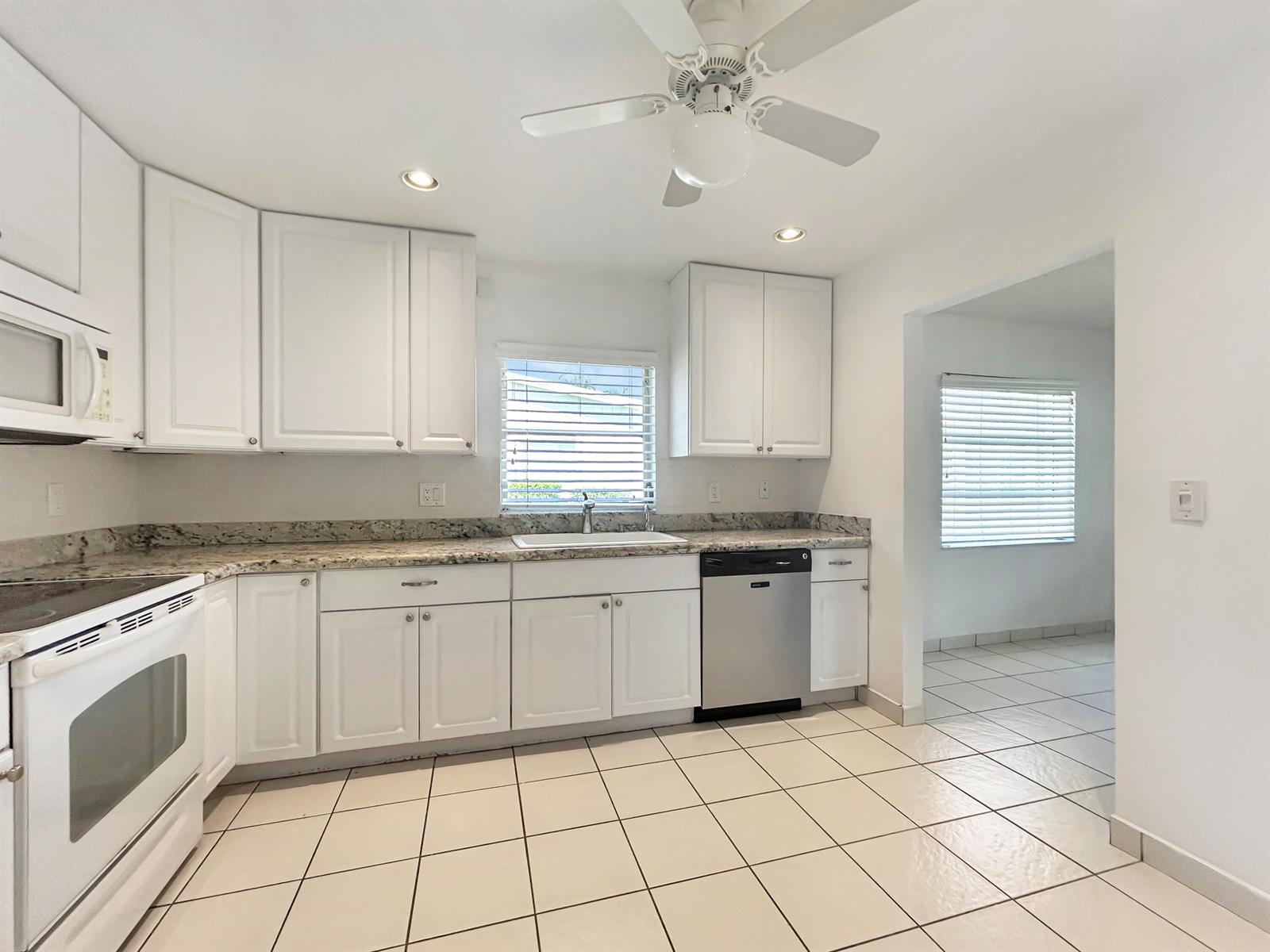 A kitchen with white cabinets, granite countertops, stainless steel appliances, and light-colored tile flooring — 6091 Dusenburg Road, Delray Beach FL 33484, DELRAY BEACH, FL