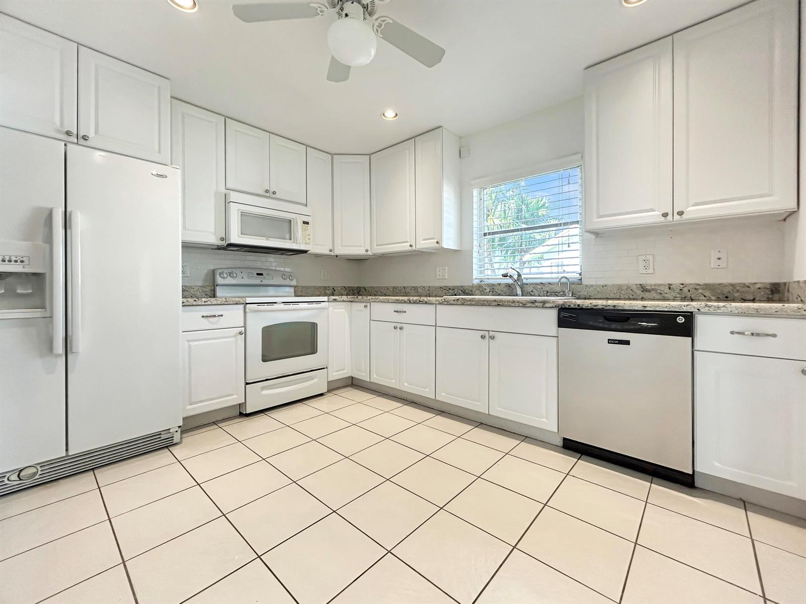 A kitchen with white cabinets, granite countertops, white appliances, and light-colored tile flooring — 6091 Dusenburg Road, Delray Beach FL 33484, DELRAY BEACH, FL
