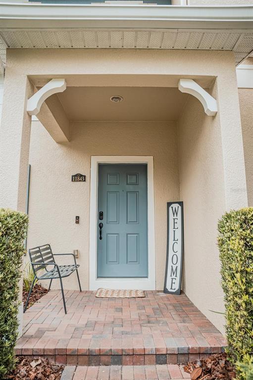 A front porch features a blue door, a metal bench, and a vertical welcome sign — 11843 DEER PATH WAY, ORLANDO, FL