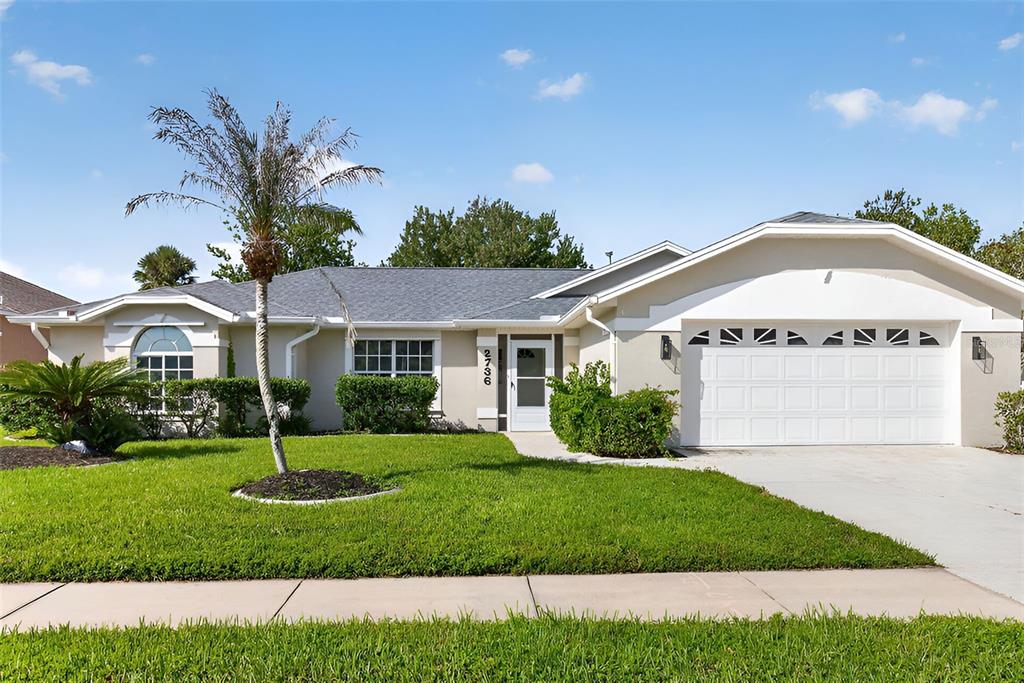 A single-story suburban house with a white garage, a palm tree, and a green lawn — 2736 TURNBULL ESTATES DRIVE, NEW SMYRNA BEACH, FL