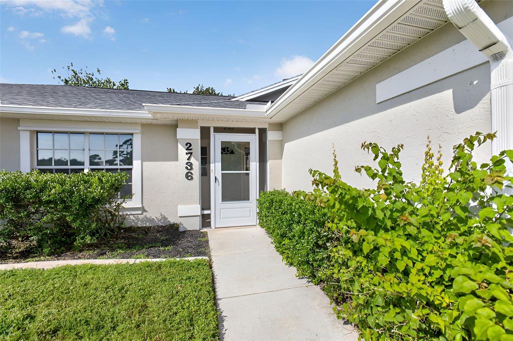 The exterior of a house features a concrete walkway leading to a white front door — 2736 TURNBULL ESTATES DRIVE, NEW SMYRNA BEACH, FL