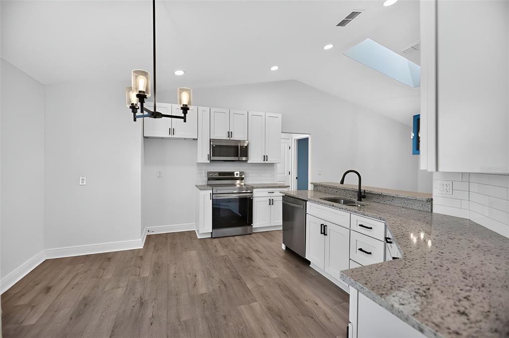 A kitchen with white cabinets, granite countertops, stainless steel appliances, and wood-look flooring — 2736 TURNBULL ESTATES DRIVE, NEW SMYRNA BEACH, FL