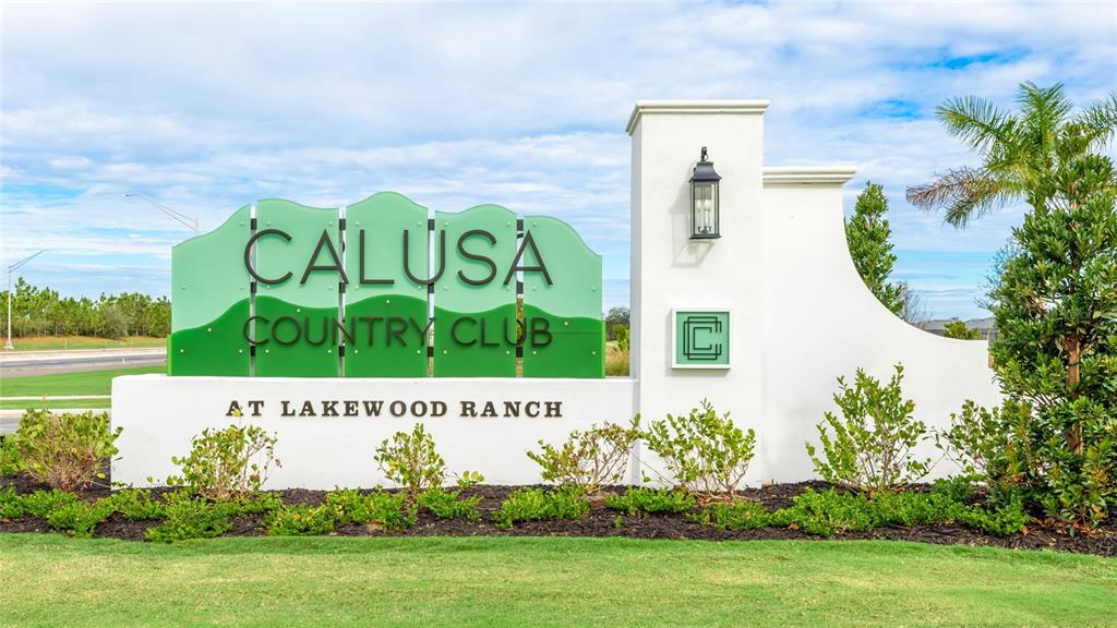 A white monument sign for Calusa Country Club stands in a landscaped grassy area — 19007 SCALLOP LOOP UNIT 204, LAKEWOOD RANCH, FL