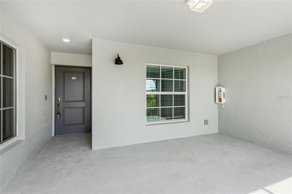A covered entryway features a gray front door, a window, and a wall-mounted fire extinguisher — 19007 SCALLOP LOOP UNIT 204, LAKEWOOD RANCH, FL