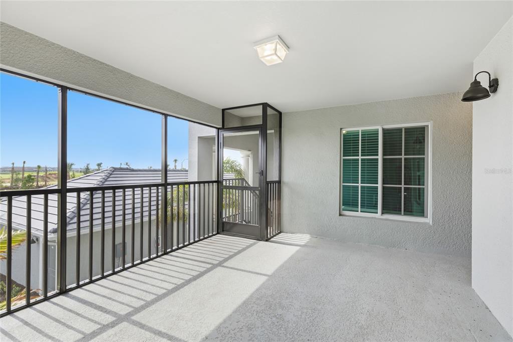 A covered balcony features a screened enclosure, metal railings, and a view of neighboring roofs — 19007 SCALLOP LOOP UNIT 204, LAKEWOOD RANCH, FL