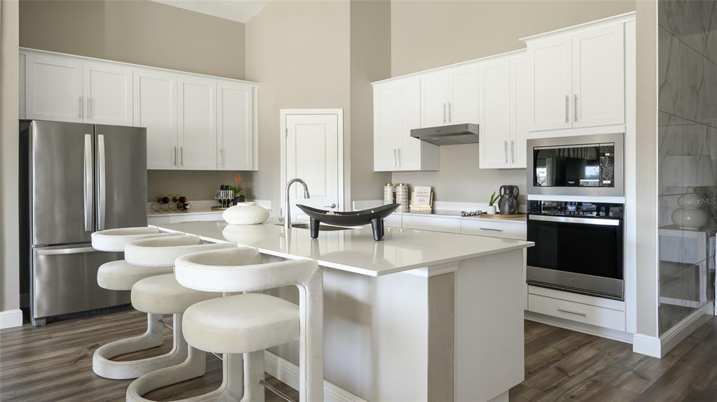 A modern kitchen features white cabinetry, stainless steel appliances, and a central island with seating — 9836 ANNUNCIATION DRIVE, WESLEY CHAPEL, FL
