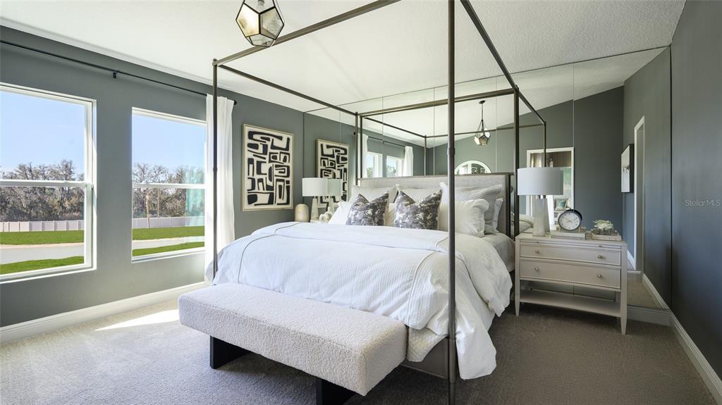 A bedroom features a four-poster bed, mirrored wall panels, and two windows overlooking a lawn — 9836 ANNUNCIATION DRIVE, WESLEY CHAPEL, FL