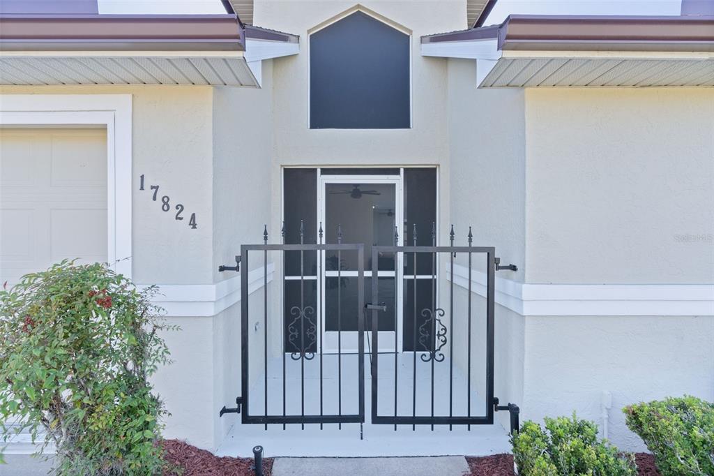 A black metal gate stands before the front entrance of a light-colored stucco house — 17824 SE 113TH TERRACE, SUMMERFIELD, FL