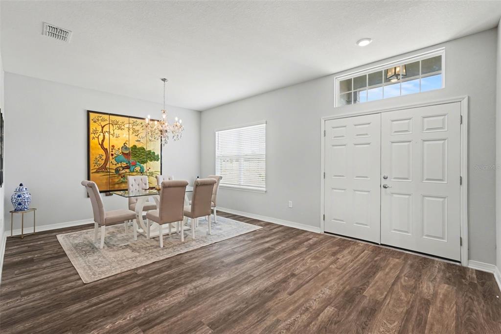 A dining room with wood-look flooring, a glass table, and a double-door entryway — 6749 ABBYWOOD LANE, ZEPHYRHILLS, FL