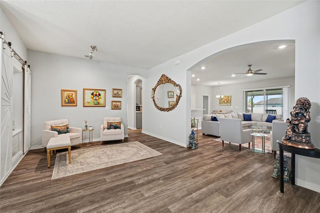A bright, open-concept living area features wood-look flooring, arched doorways, and a formal seating space — 6749 ABBYWOOD LANE, ZEPHYRHILLS, FL