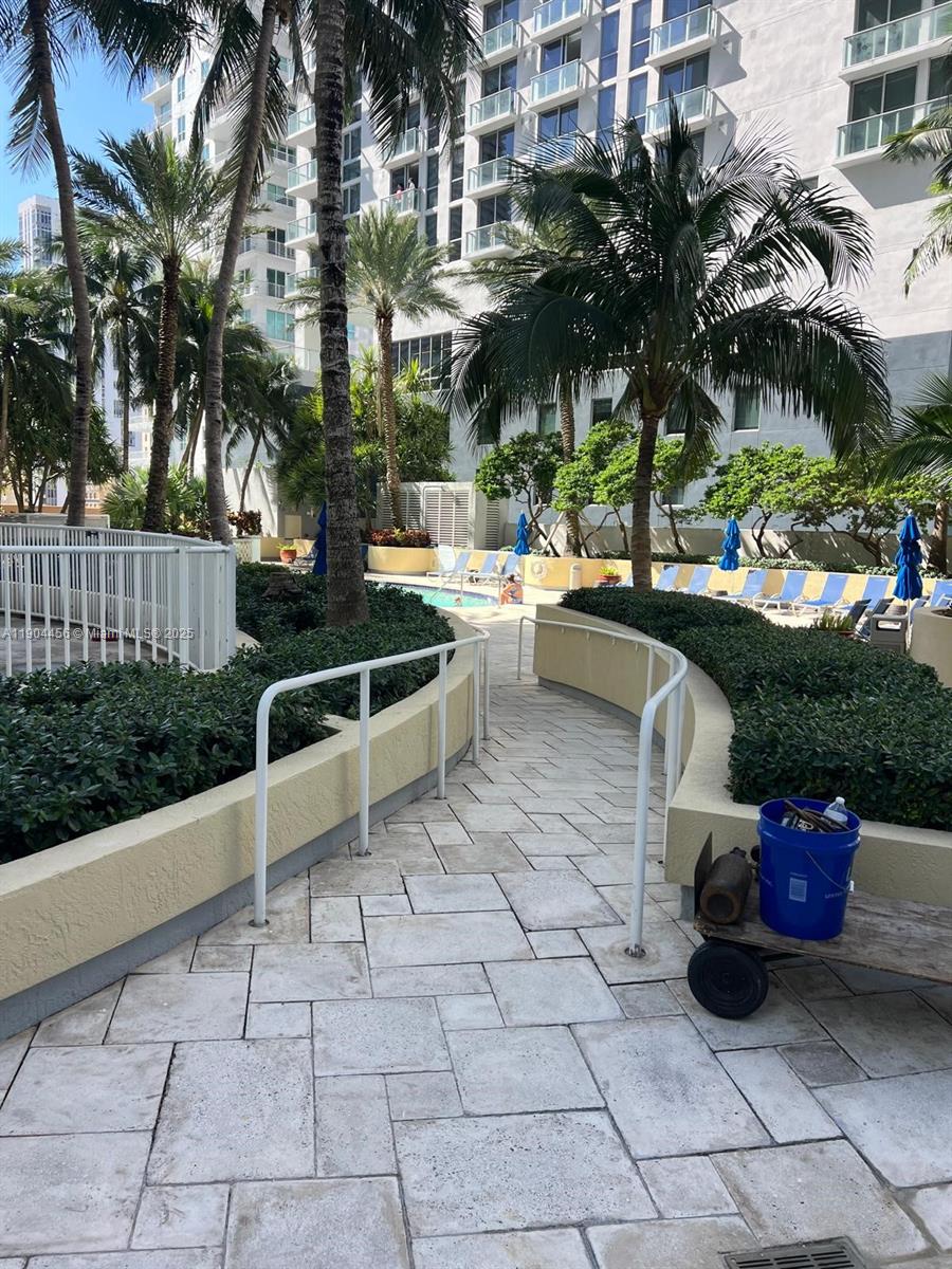 A paved walkway with white railings leads toward a swimming pool area with lounge chairs — 244 Biscayne Blvd # 308, Miami FL 33132, MIAMI, FL