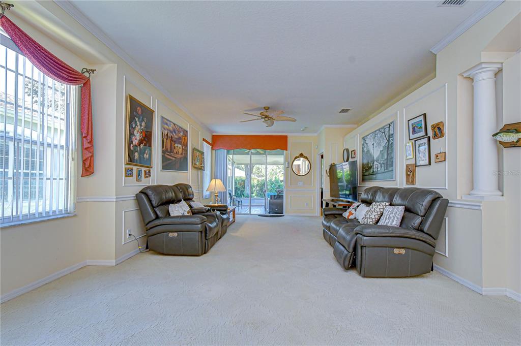 A living room with beige carpet, two leather sofas, wall molding, and a sliding glass door — 6073 SANDHILL RIDGE DRIVE, LITHIA, FL