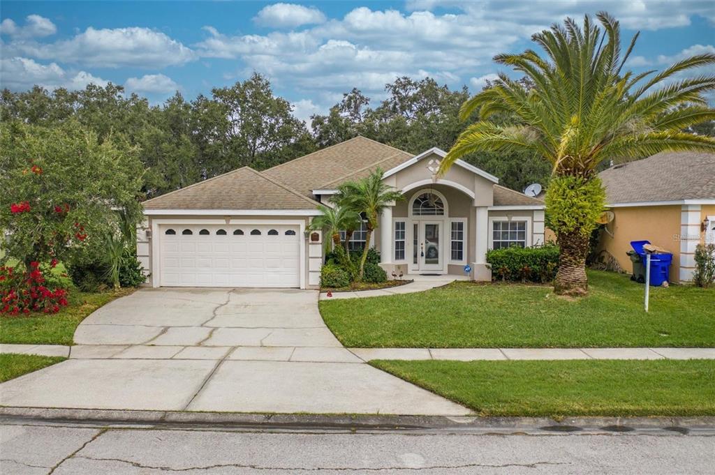 A single-story suburban house with a two-car garage, arched entryway, and a large palm tree — 2111 EAGLEVIEW COURT, KISSIMMEE, FL