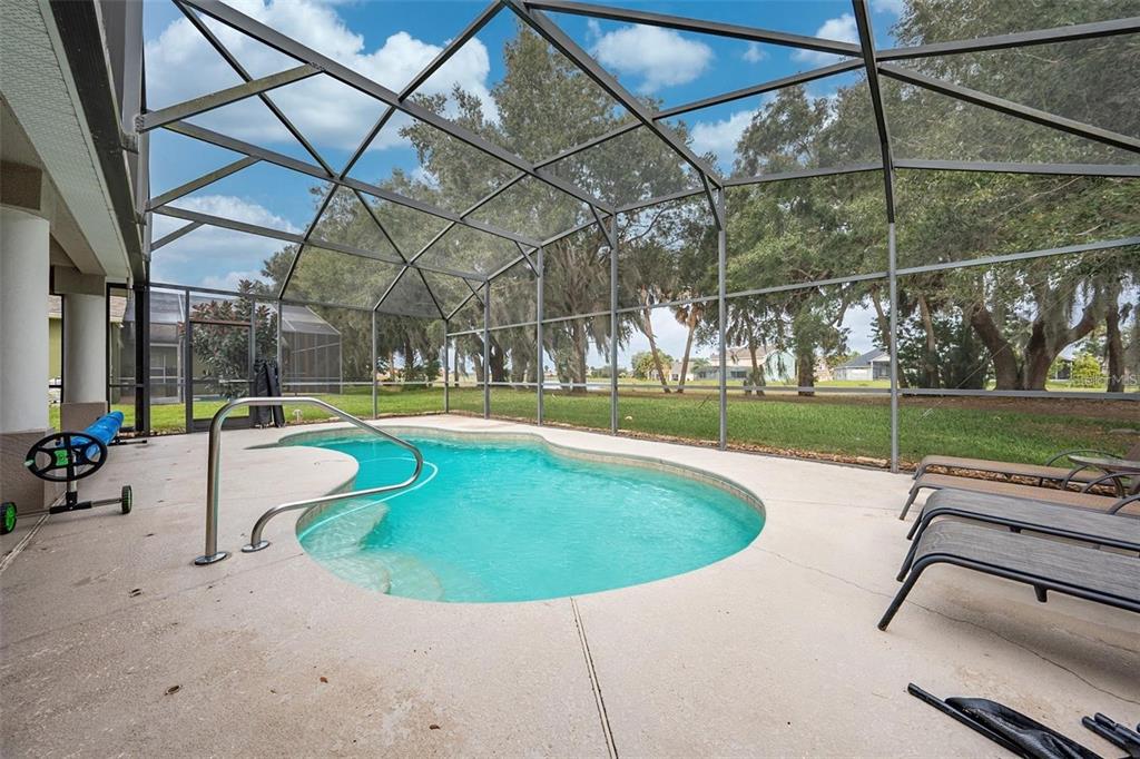 A screened-in patio features a kidney-shaped swimming pool, lounge chairs, and a view of trees — 2111 EAGLEVIEW COURT, KISSIMMEE, FL