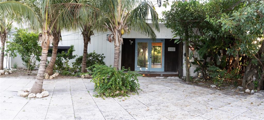 The exterior of a building features a paved driveway, palm trees, and double glass doors — 300 GARDEN LANE, SARASOTA, FL