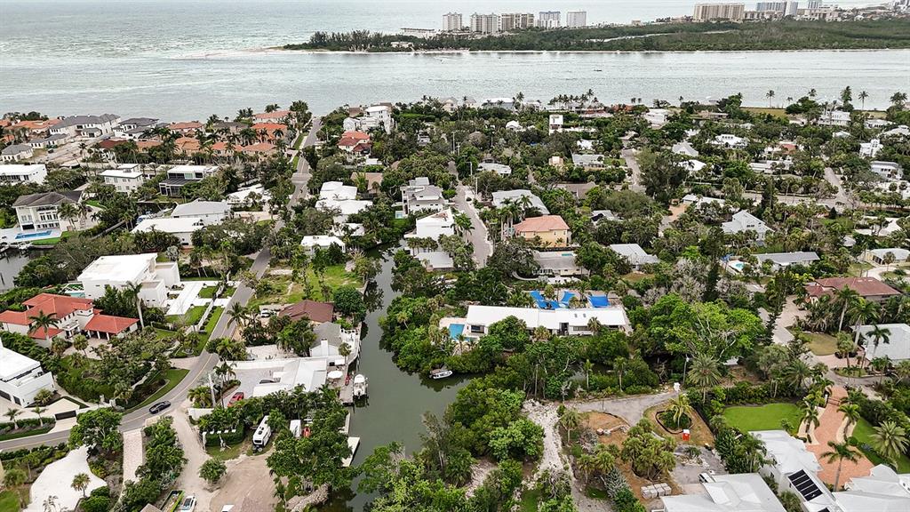 An aerial view shows a coastal neighborhood with houses, lush vegetation, and a narrow waterway — 300 GARDEN LANE, SARASOTA, FL