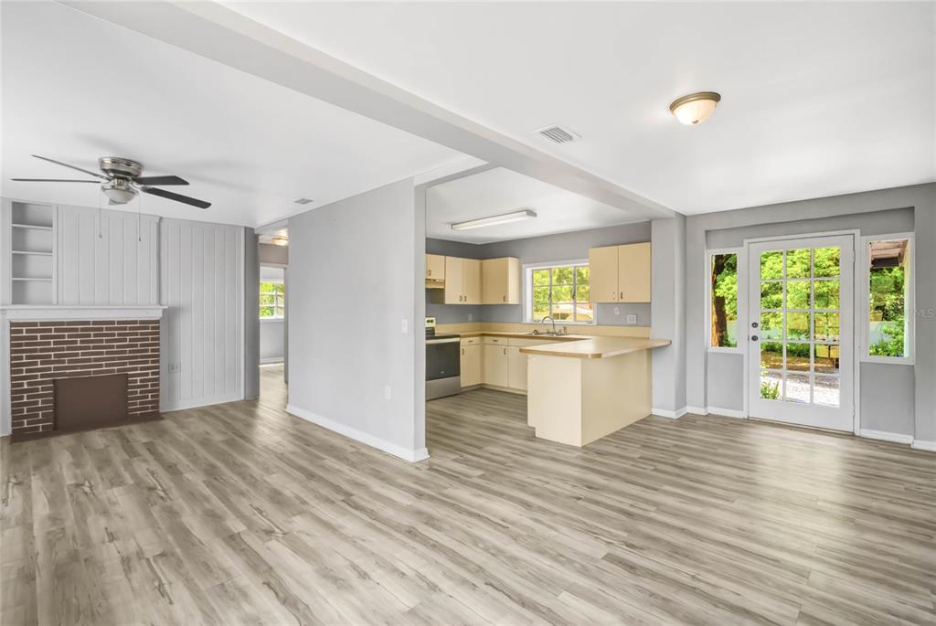 An open-concept living area with wood-look flooring, a brick fireplace, and an adjacent kitchen — 322 N FRANKFORT AVENUE, DELAND, FL