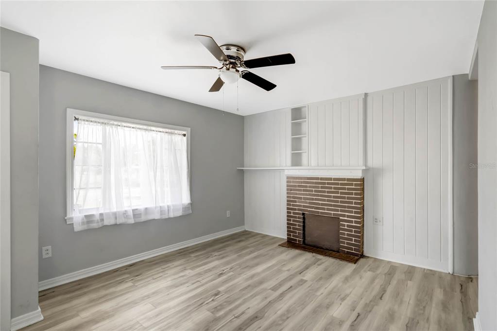 A living room features light gray walls, wood-look flooring, a ceiling fan, and a brick fireplace — 322 N FRANKFORT AVENUE, DELAND, FL