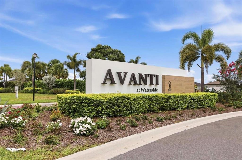 A white monument sign for Avanti at Waterside stands in a landscaped garden area — 6391 WATERSTONE PLACE, SARASOTA, FL