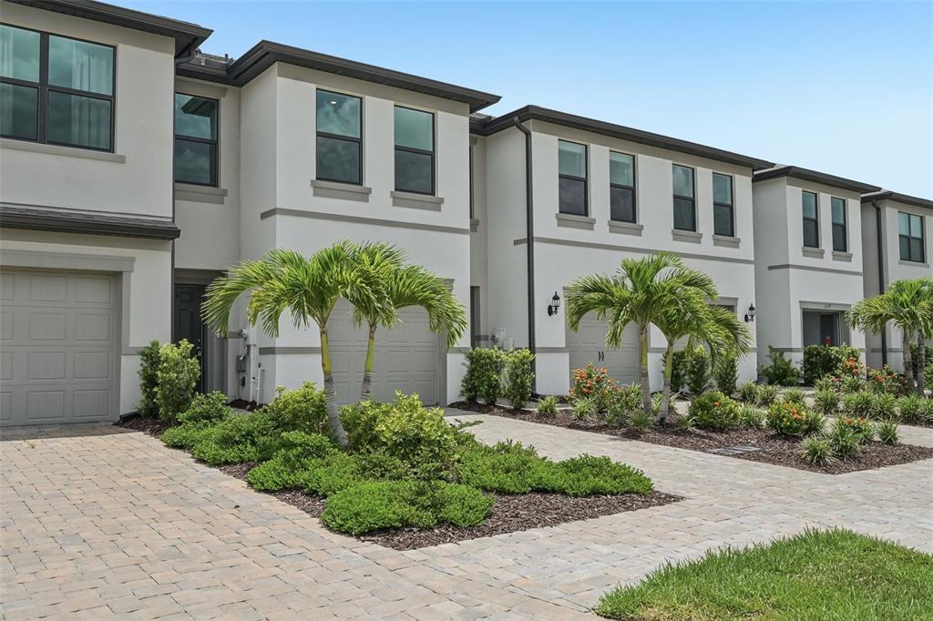 A row of modern two-story townhouses features light-colored stucco exteriors, paver driveways, and palm trees — 6391 WATERSTONE PLACE, SARASOTA, FL