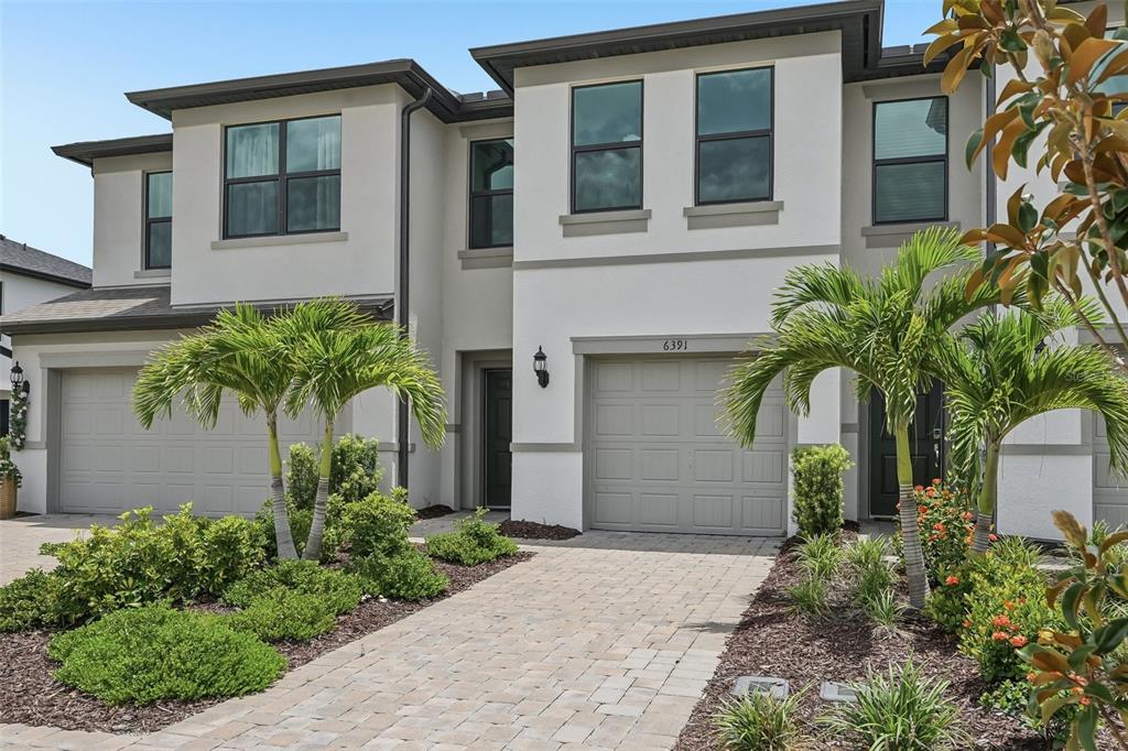 A two-story townhouse exterior features a paved driveway, two garages, and palm trees — 6391 WATERSTONE PLACE, SARASOTA, FL