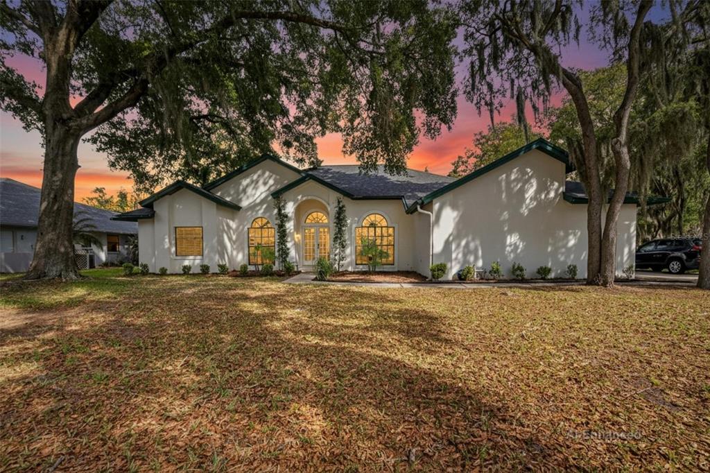 A single-story white house with arched windows and a dark roof under a sunset sky — 2904 PINE CLUB DRIVE, PLANT CITY, FL