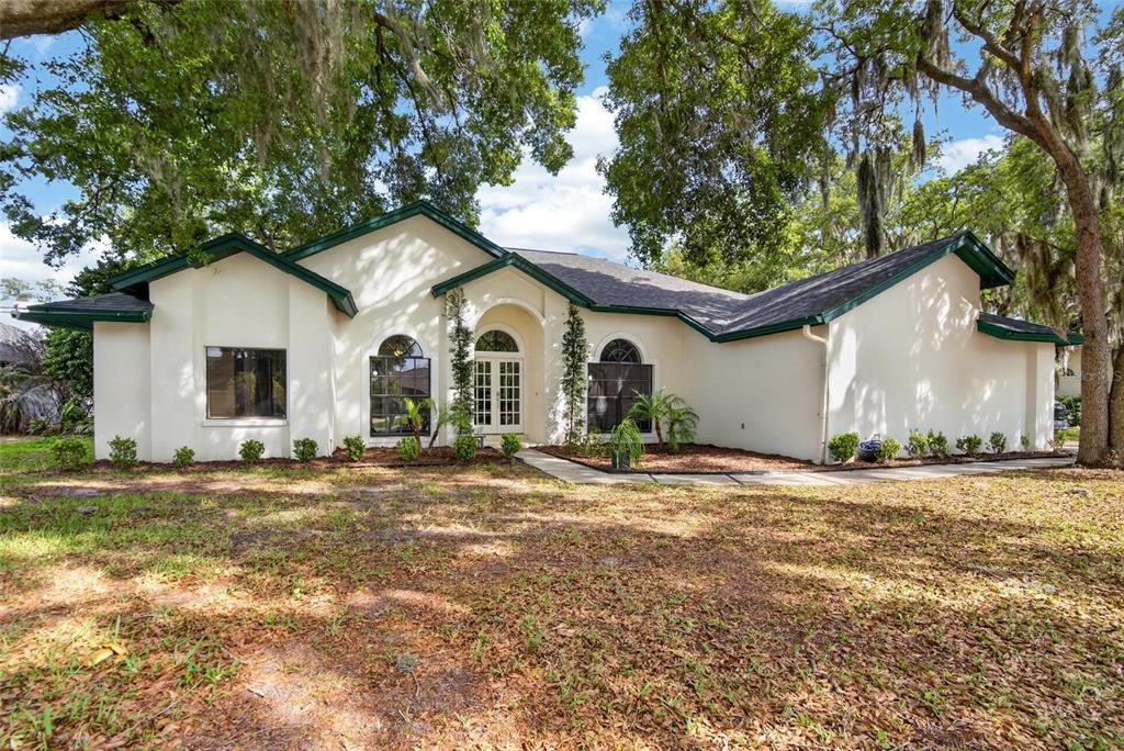 A single-story house with white stucco walls, dark green trim, and arched windows — 2904 PINE CLUB DRIVE, PLANT CITY, FL