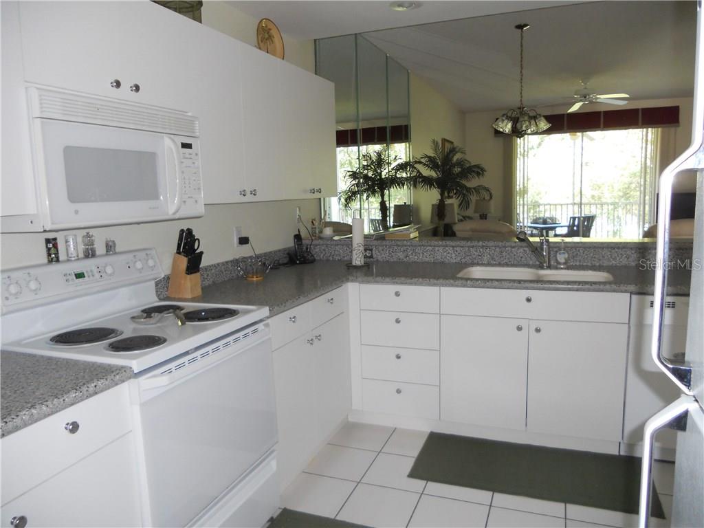 A white kitchen features granite countertops, white cabinetry, a white stove, and a mirrored wall — 8750 OLDE HICKORY AVENUE UNIT 9204, SARASOTA, FL