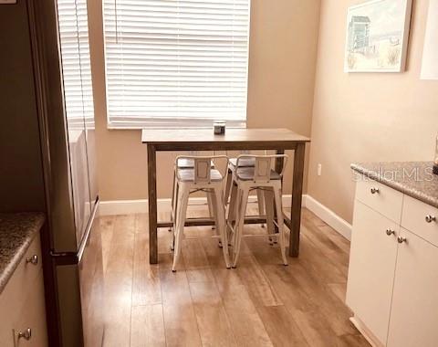 A small dining area features a wooden table with two white metal stools on wood flooring — 8750 OLDE HICKORY AVENUE UNIT 9204, SARASOTA, FL