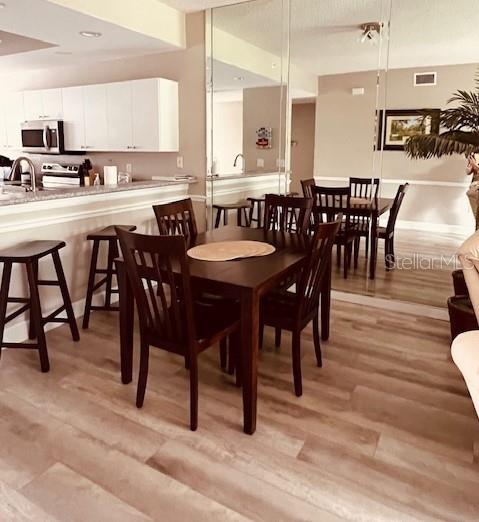 A dining area with a wooden table and chairs sits adjacent to a kitchen with stools — 8750 OLDE HICKORY AVENUE UNIT 9204, SARASOTA, FL