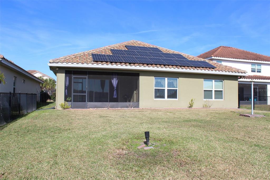 The rear exterior of a house features a tiled roof with solar panels and a screened-in porch — 1408 LANIER POINT PLACE, KISSIMMEE, FL