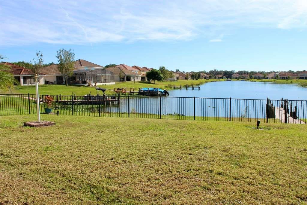 A grassy backyard overlooks a lake with several houses and private docks in the distance — 1408 LANIER POINT PLACE, KISSIMMEE, FL