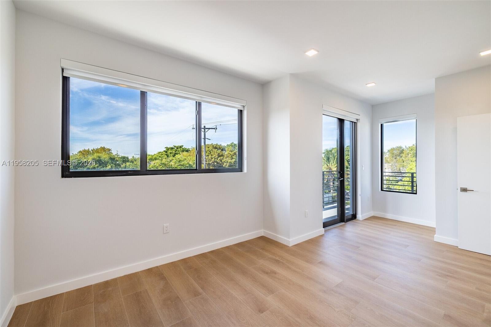 An empty room features light wood-look flooring, white walls, large windows, and a glass balcony door — 1376 SW 4th St # 401, Miami FL 33135, MIAMI, FL