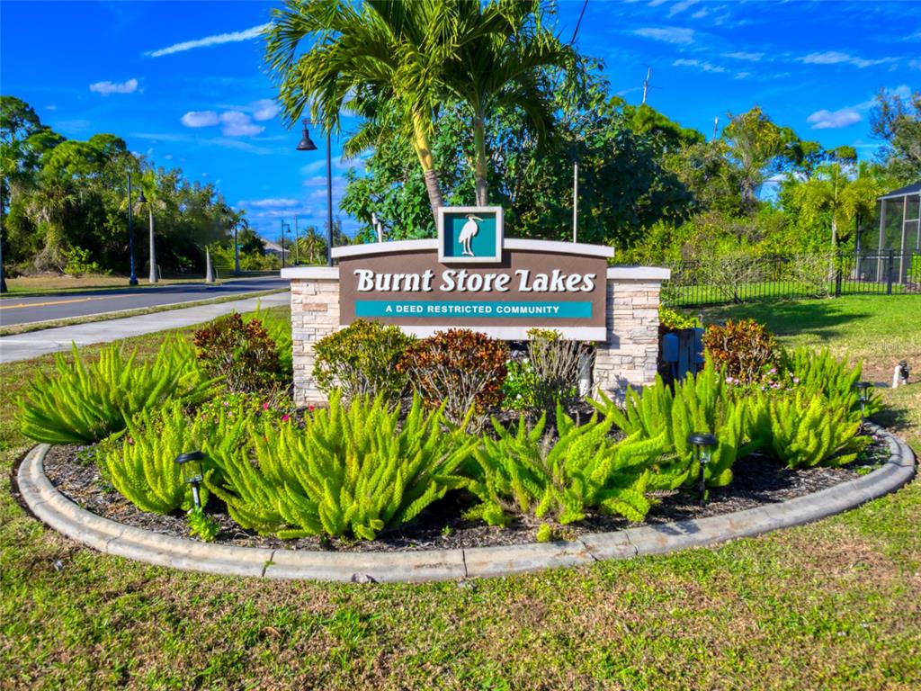 A stone monument sign for Burnt Store Lakes stands in a landscaped garden bed — 17262 COMINGO LANE, PUNTA GORDA, FL
