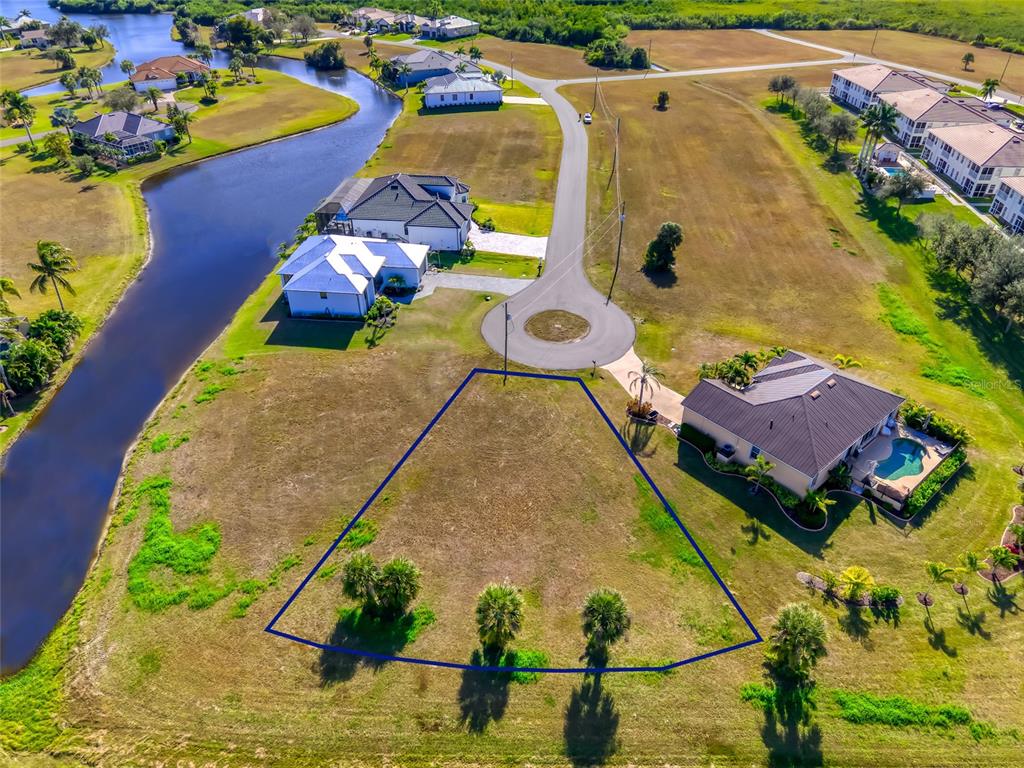 An aerial view shows a vacant, trapezoidal residential lot situated next to a canal — 17262 COMINGO LANE, PUNTA GORDA, FL