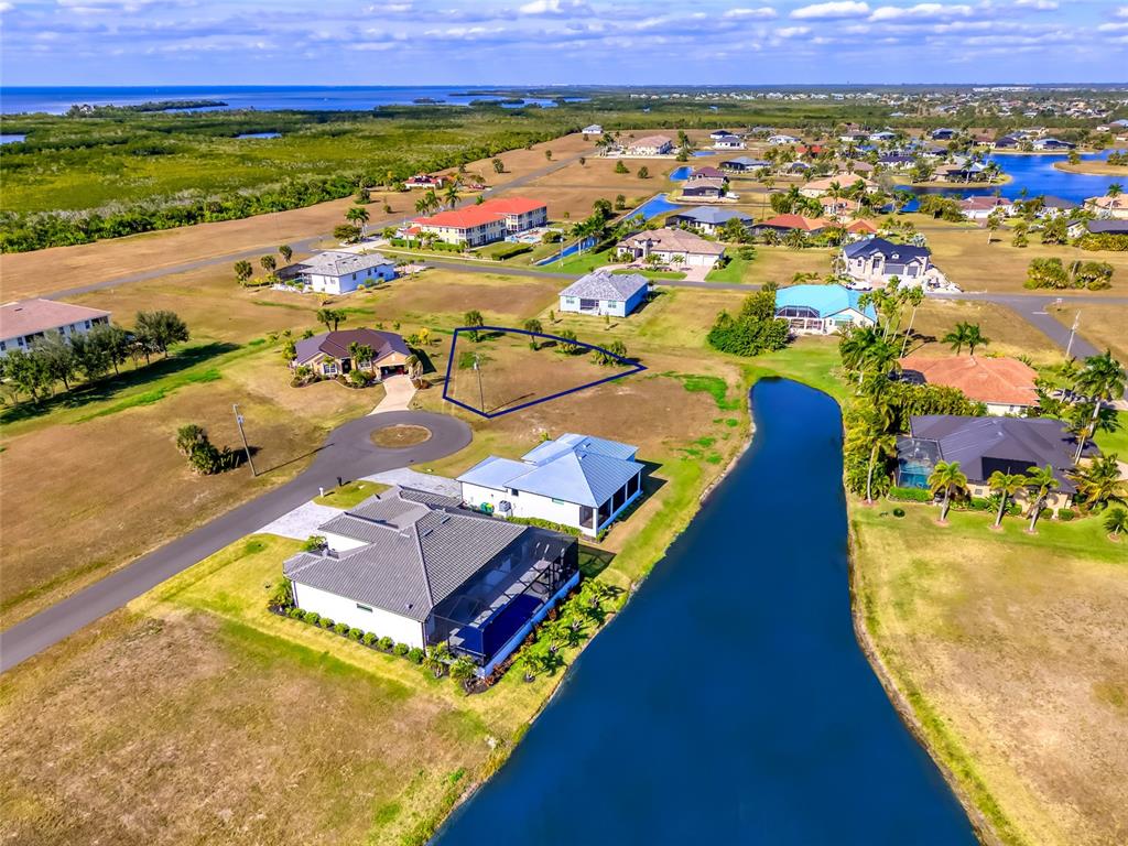 An aerial view shows a vacant, triangular residential lot surrounded by houses and a canal — 17262 COMINGO LANE, PUNTA GORDA, FL