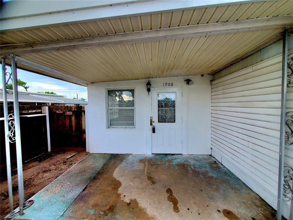 A covered concrete porch leads to a white front door with a decorative glass insert — 1908 SHADY COVE DRIVE, HOLIDAY, FL