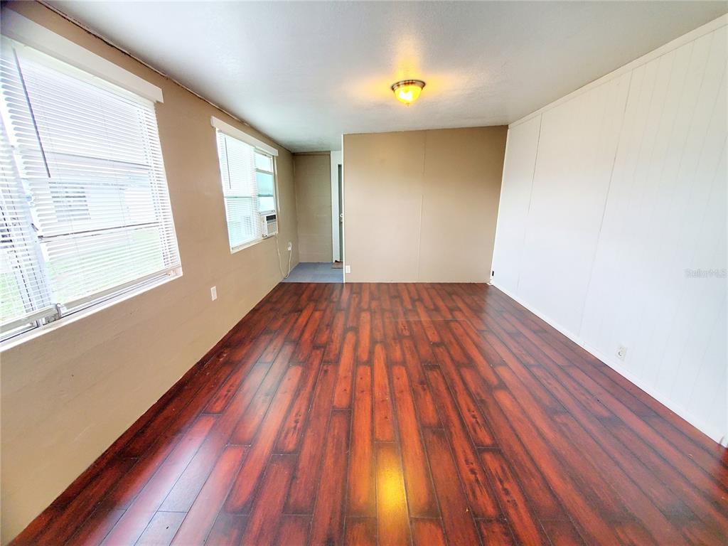 An empty room features dark wood-look flooring, white paneled walls, and two windows with blinds — 1908 SHADY COVE DRIVE, HOLIDAY, FL
