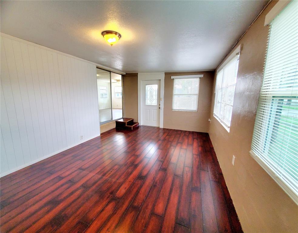 A sunroom features dark wood-look flooring, white paneled walls, a ceiling light, and a door — 1908 SHADY COVE DRIVE, HOLIDAY, FL