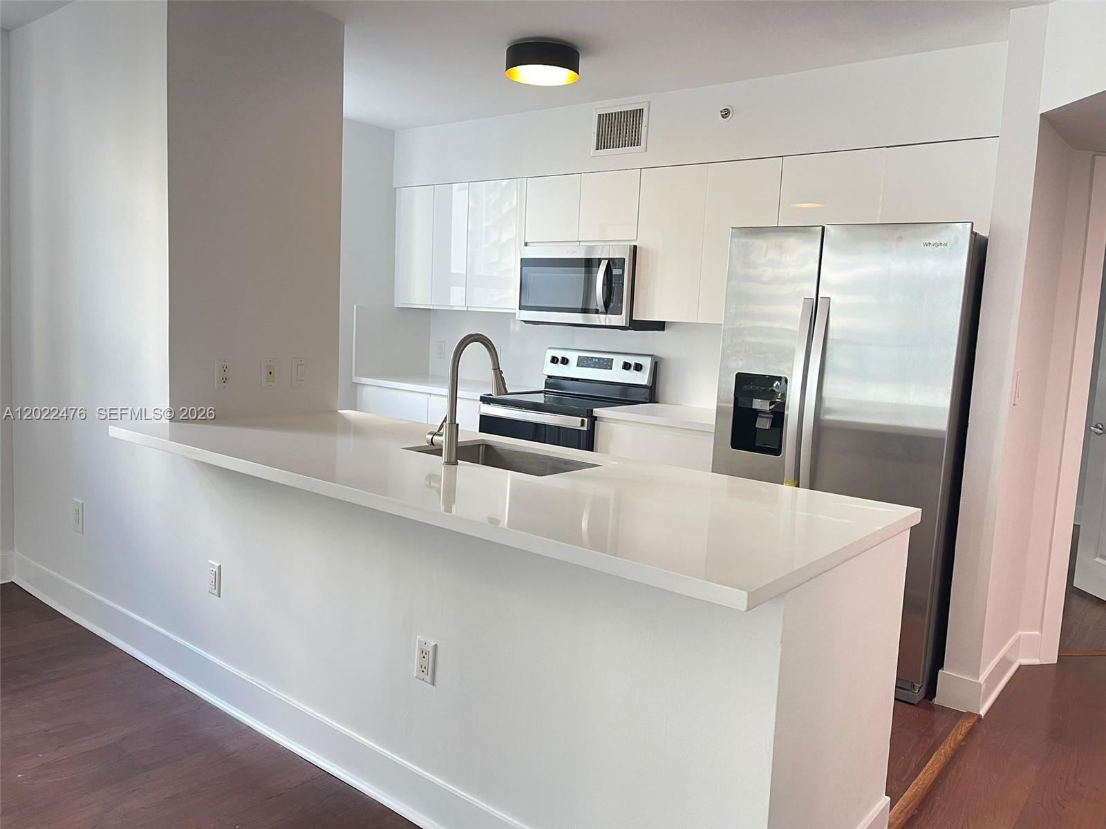 A modern kitchen features white cabinets, stainless steel appliances, and a white quartz breakfast bar — 1155 Brickell Bay Dr # 1102, Miami FL 33131, MIAMI, FL